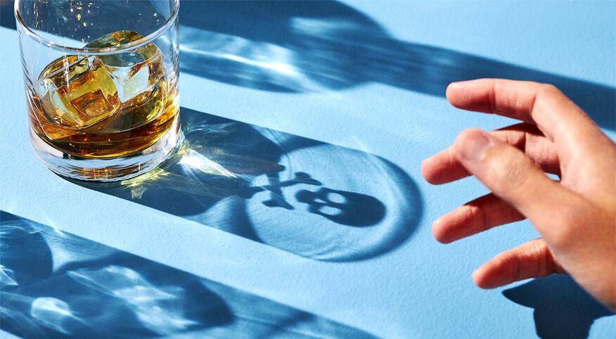Hand reaching for alcoholic beverage with shadow casted on table of skull and bones