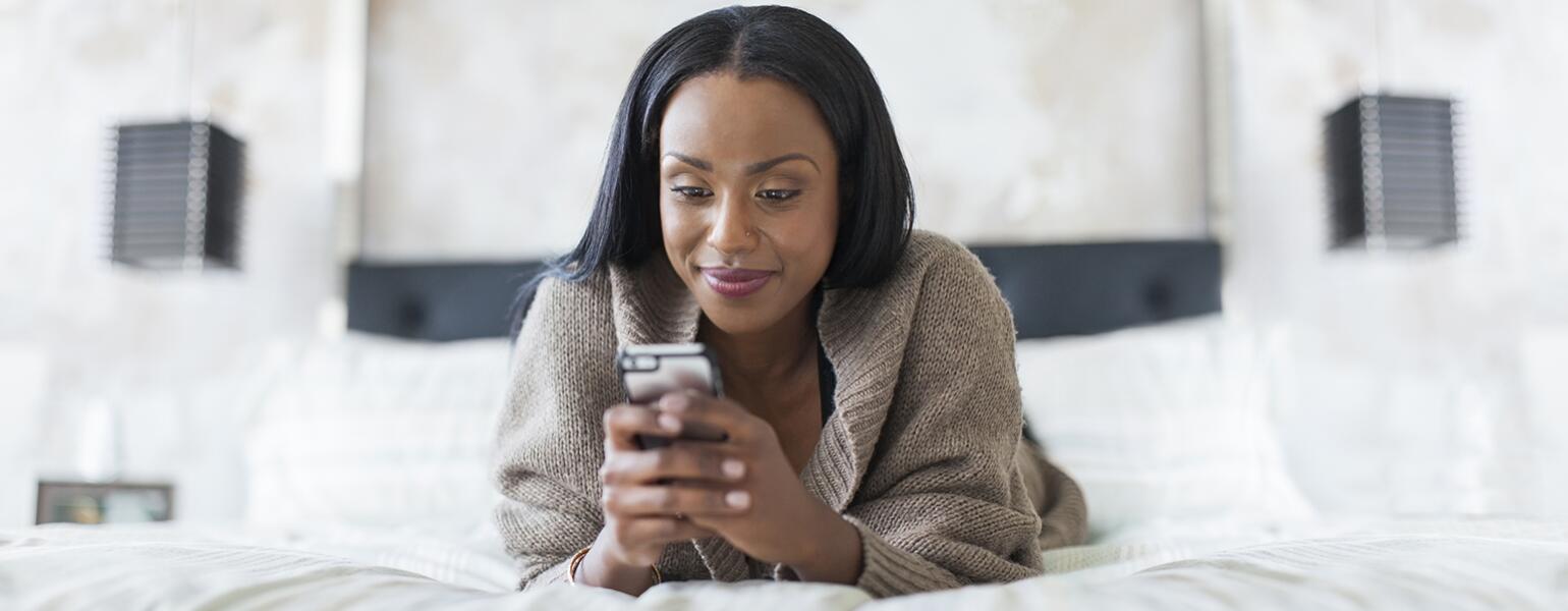 A picture of a woman texting on her cellphone while lying in bed.
