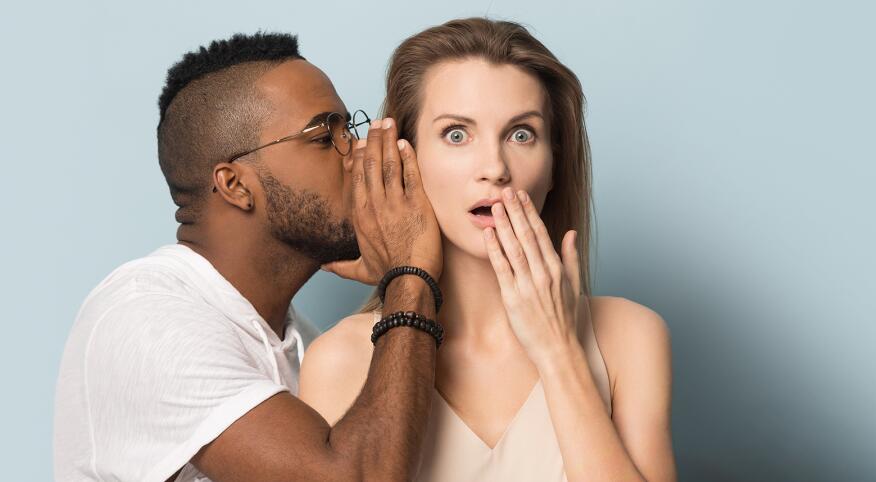 African American man tell secret to shocked caucasian female