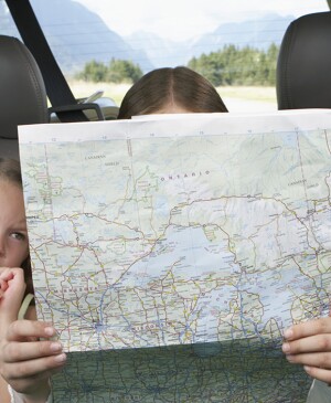 Three girls sitting on rear seat of car on road trip looking at a map