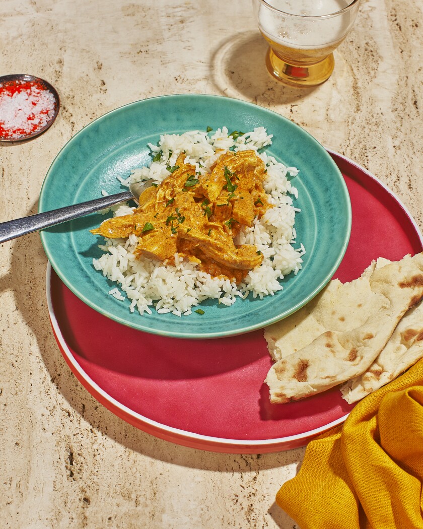 Indian butter chicken on a colorful plate served with naan bread and beer