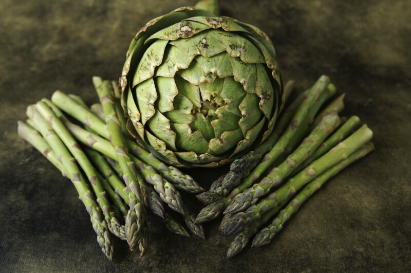 A still life of an aritchoke and asparagus on a textured background