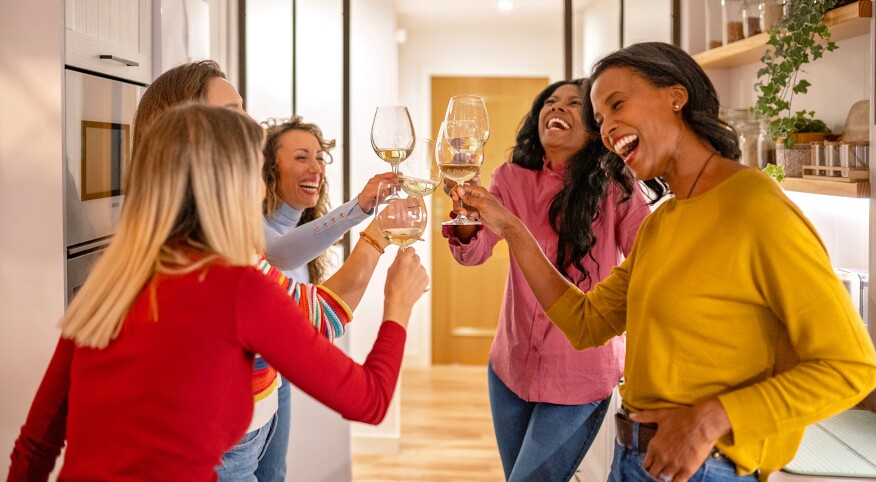 Five female friends gathered in the kitchen sharing laughs and wine