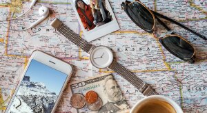 Photo of a U.S. map with miscellaneous travel items on top like a watch, sunglasses, headphones, money, cell phone and polaroid photo.