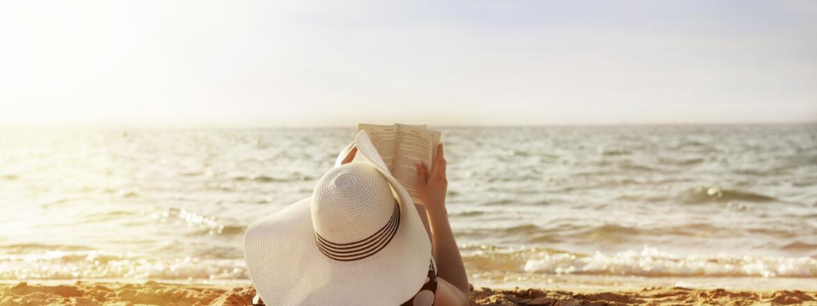 woman laying on towel reading on beach in the sun