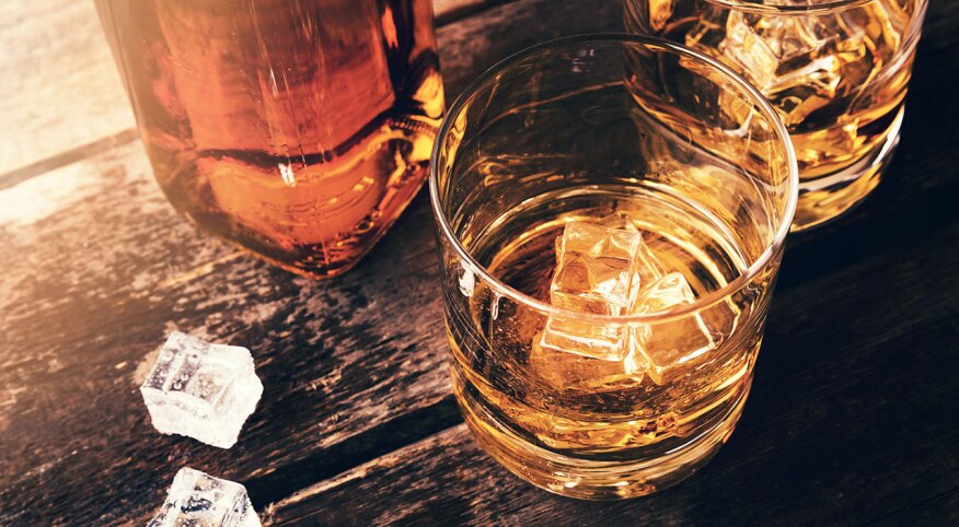 Whiskey bottle and glasses with ice cubes on old wooden table