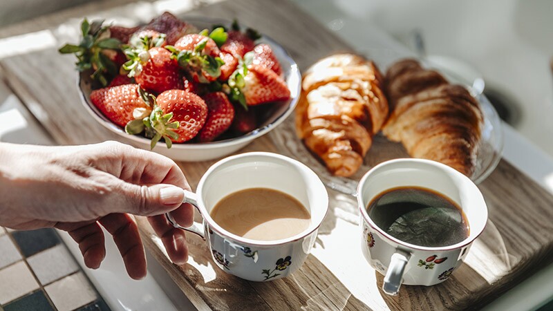 A close-up view of two cups of coffee, strawberries and croissants