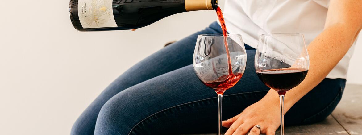 Woman sitting on a bench pouring red wine into a glass