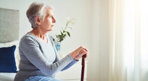 Mature woman looking thoughtful while holding a walking stick at home