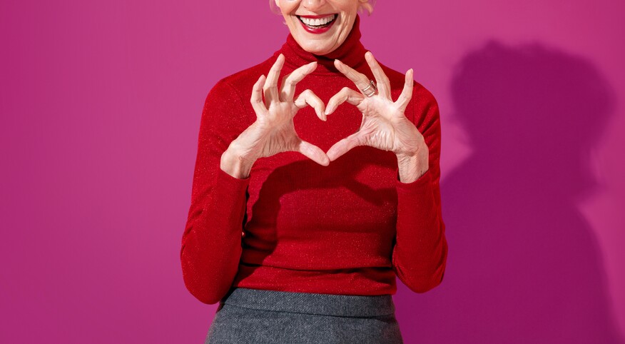 Beautiful mature woman shows heart symbol, shapes love sign with hands