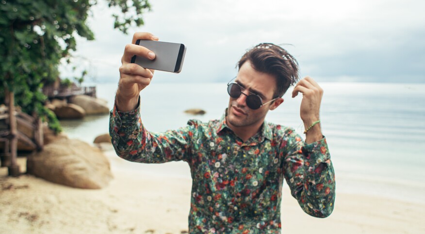 Narcissistic man taking photo of himself on the beach with his phone.