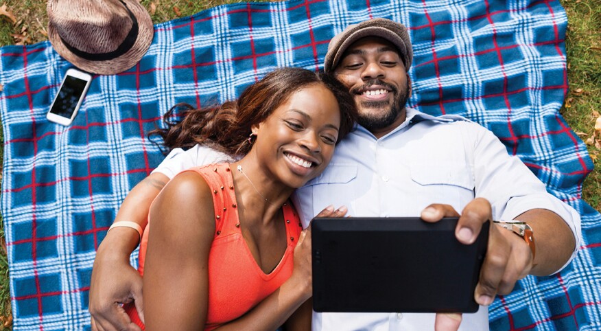 Couple lying on grass watching movie on tablet