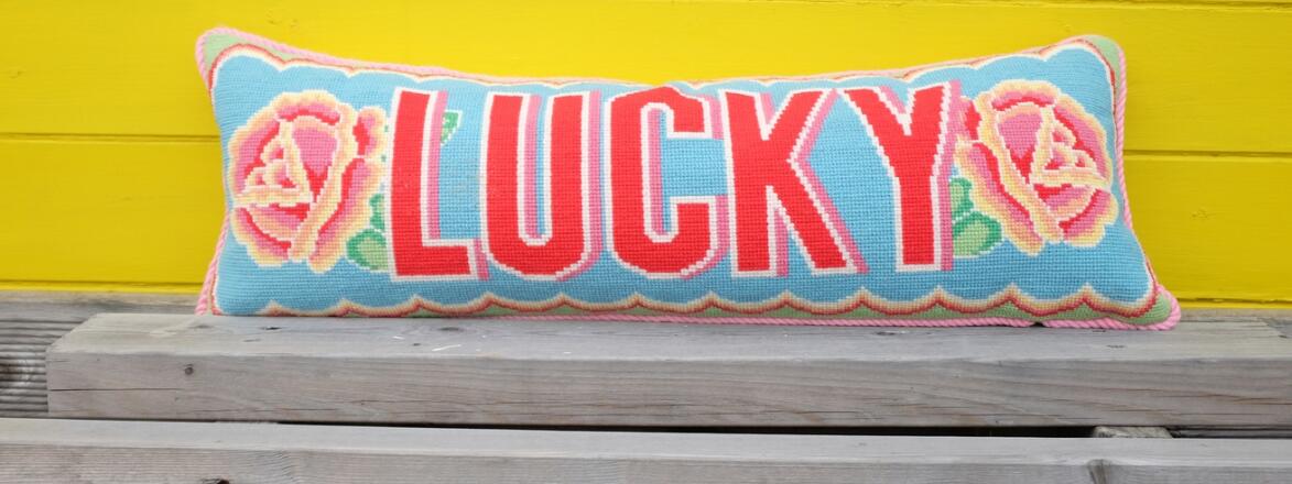 Needlepoint pillow with the word "lucky" on it by Emily Peacock