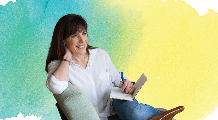 Jean Chatzky sitting in a chair writing in a notebook with water color background