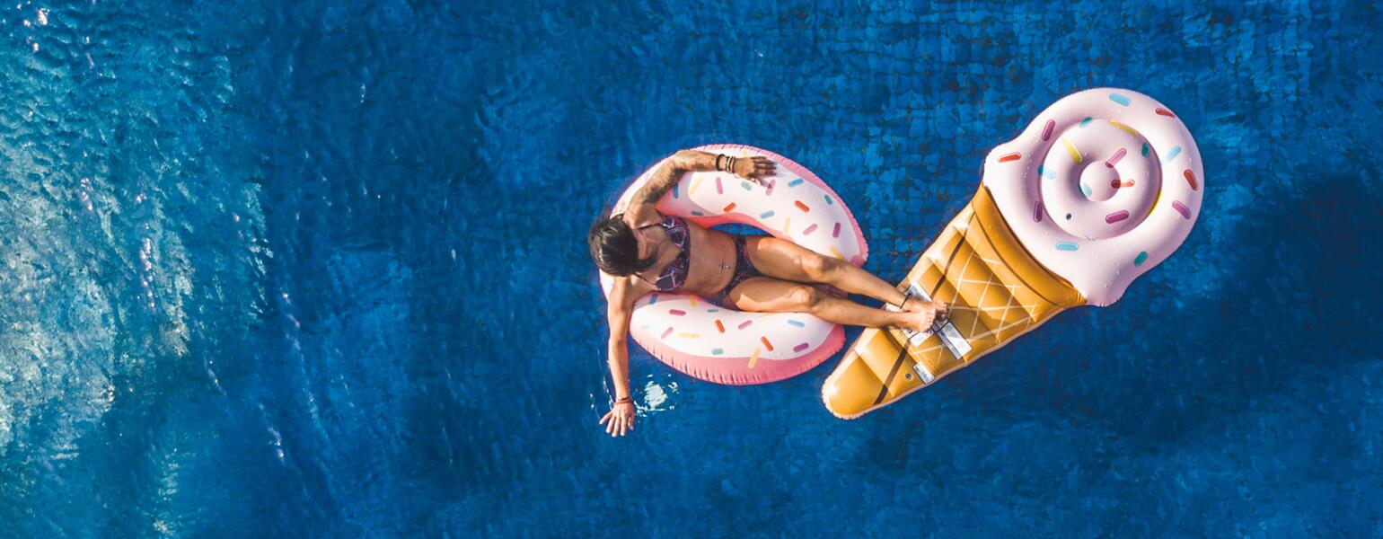 Young Woman Floating In Big Swimming Pool On Inflatable Donut