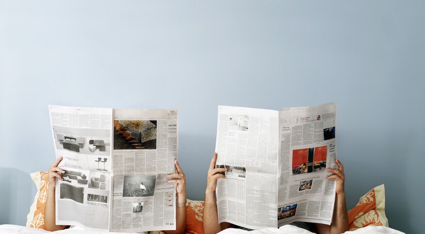 young couple laying in bed reading separate newspapers