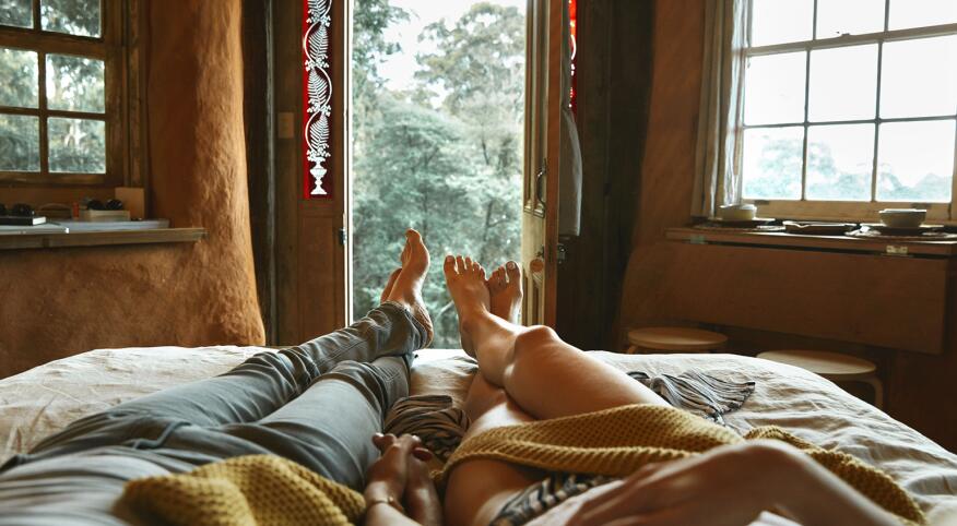 An image of a man and women's legs in bed, where they are lounging together and holding hands.