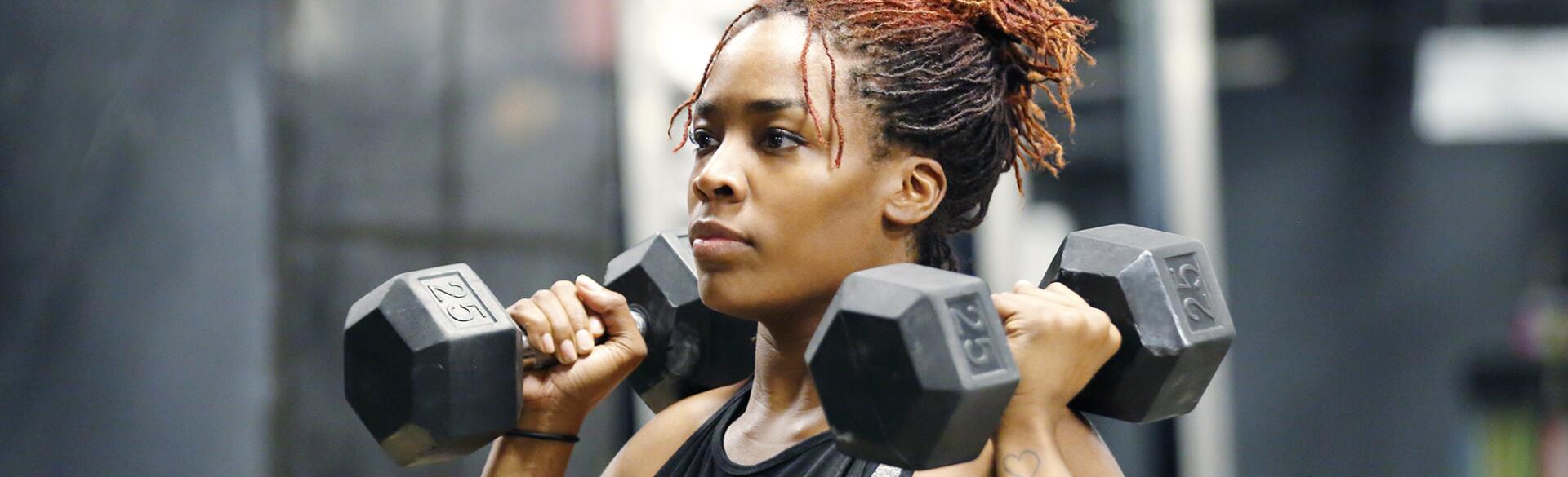 Fit, young African American woman working out with hand weights in a fitness gym.