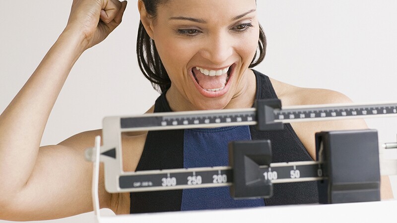 A woman smiling as she weighs herself on a scale