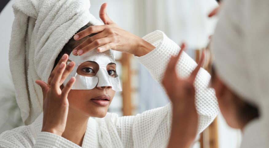 Woman looking in bathroom mirror and putting on beauty face mask