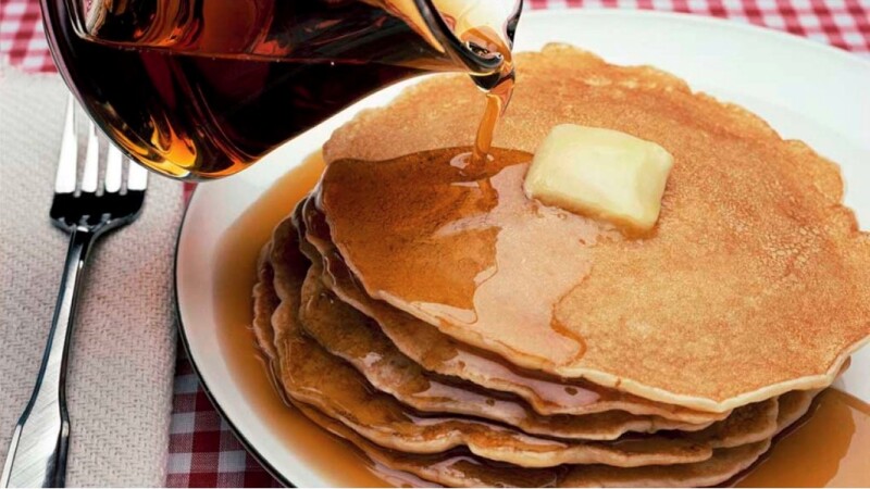 A close-up view of maple syrup being poured onto pancakes on a plate