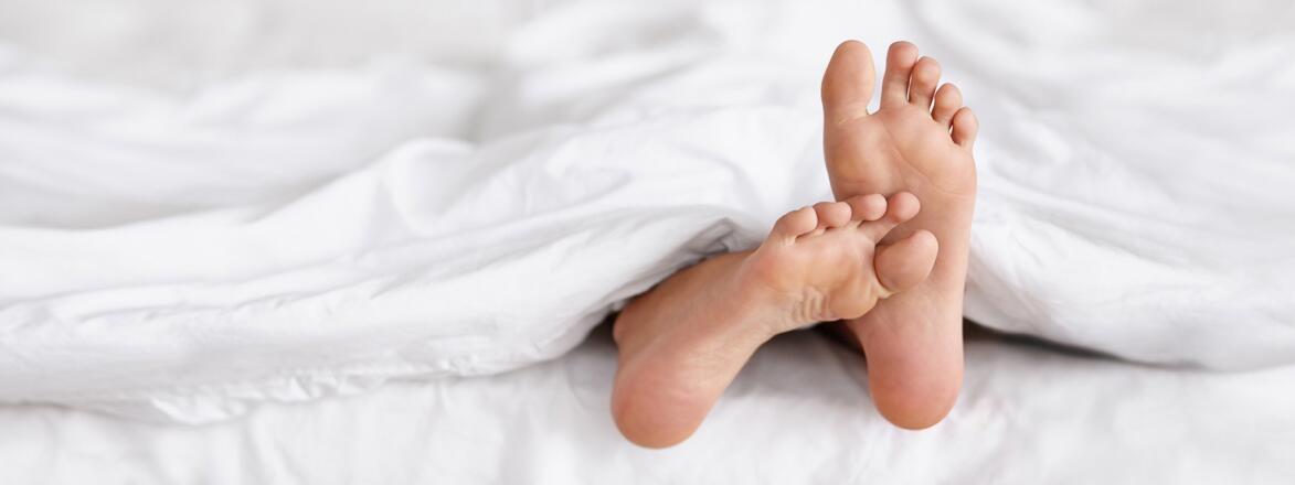 An image depicting two feet sticking out from underneath a white blanket in bed.