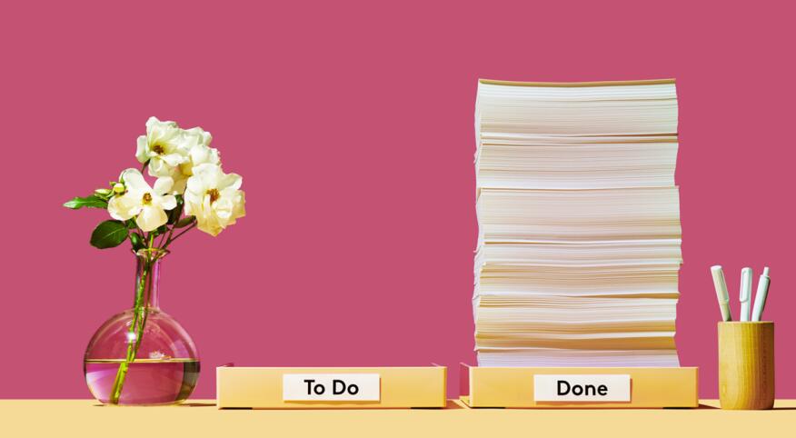 Organized desk with stack of papers with to do list and done list on pink background