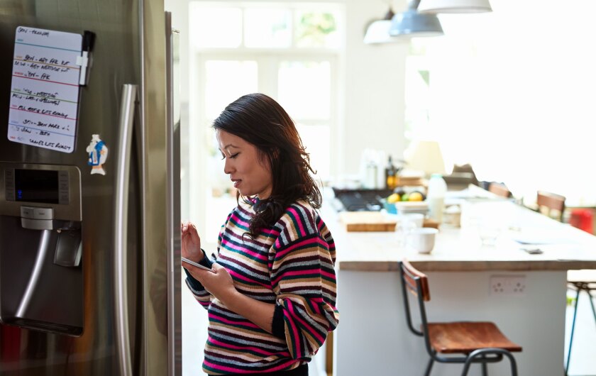 Get-busy-woman-reading-her-phone-looking-into-refrigerator_GettyImages-1153698765.jpg