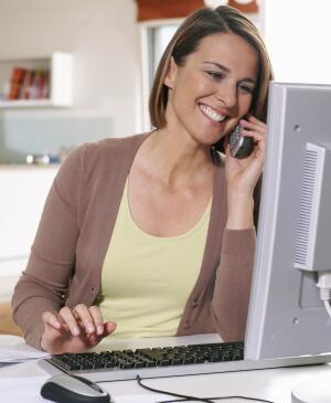 Smiling woman sitting at computer holding telephone