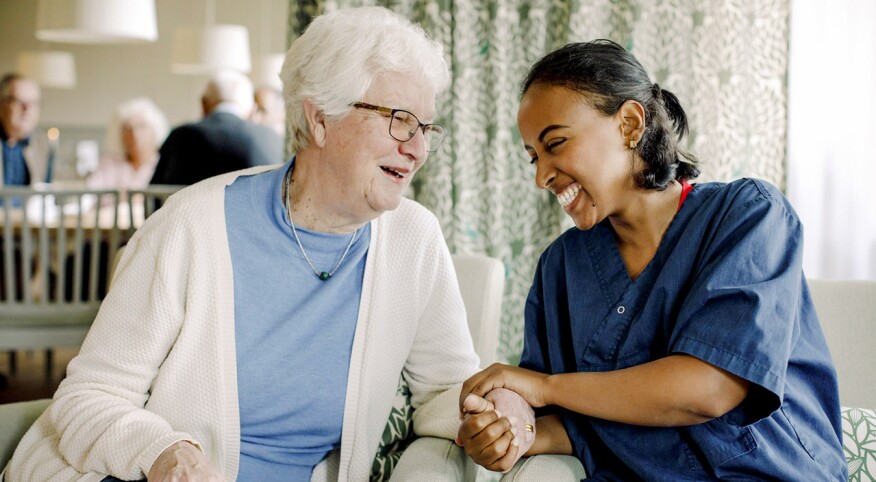Cheerful female nurse holding hand of senior woman sitting at retirement home