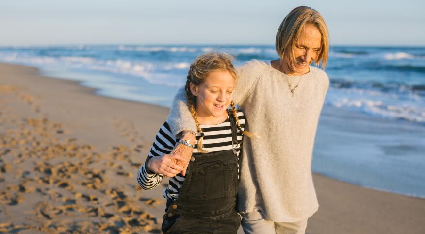 Grandmother And Her Granddaughter Walking Together On The Beach In Autumn.