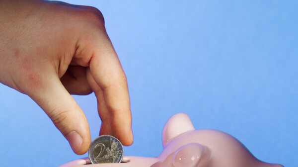 Close-up of human hand inserting two euro coin into piggy bank
