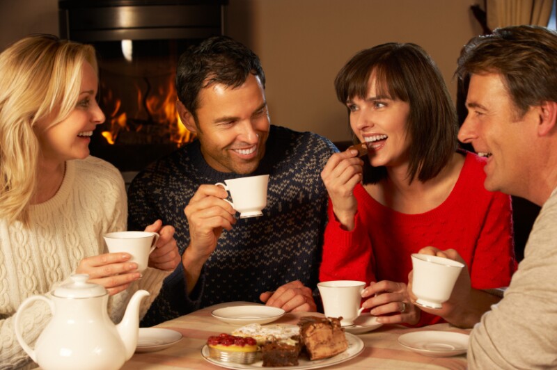 Group Of Middle Aged Couples Enjoying Tea And Cake Together