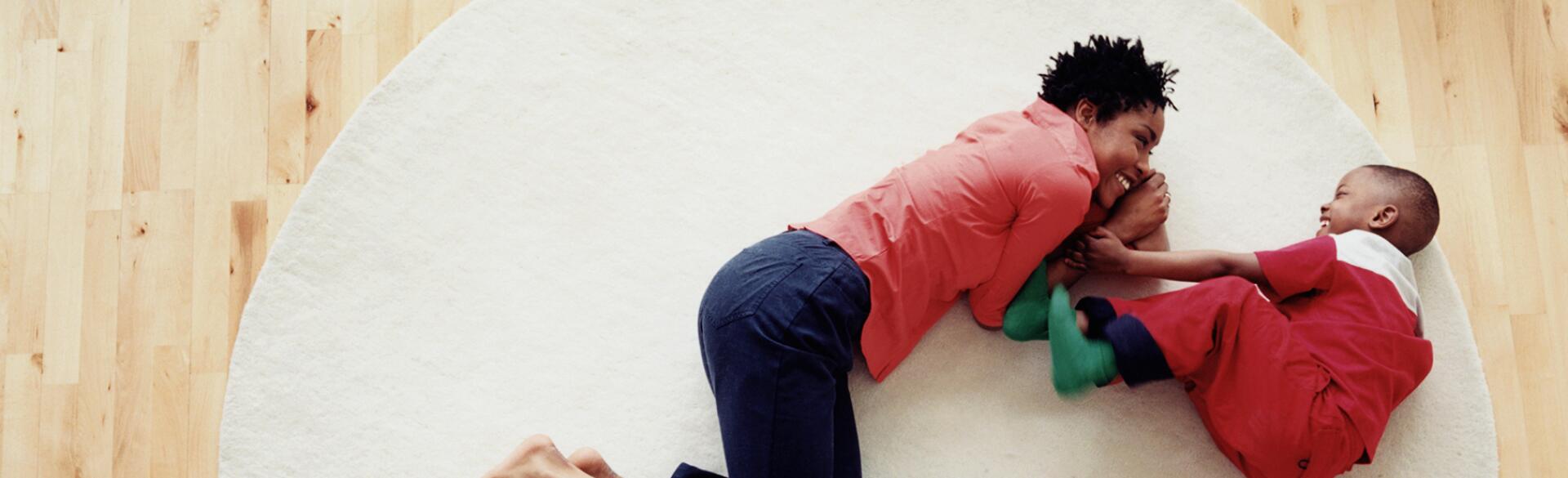 Mother and son (3-5) lying on rug, smiling, overhead view
