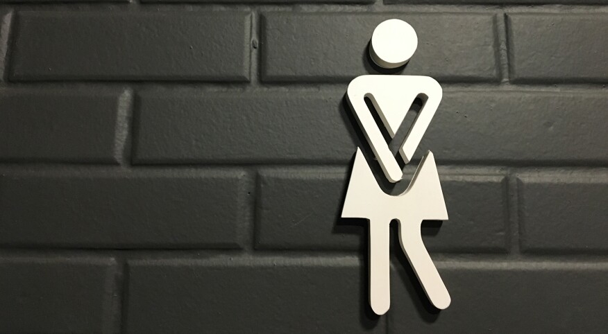 White urinary urgency sign for women on bathroom entrance with black brick wall