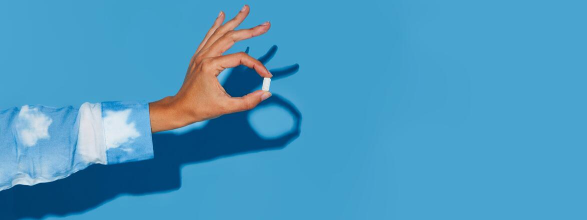 Hand holding out a vitamin on a blue background