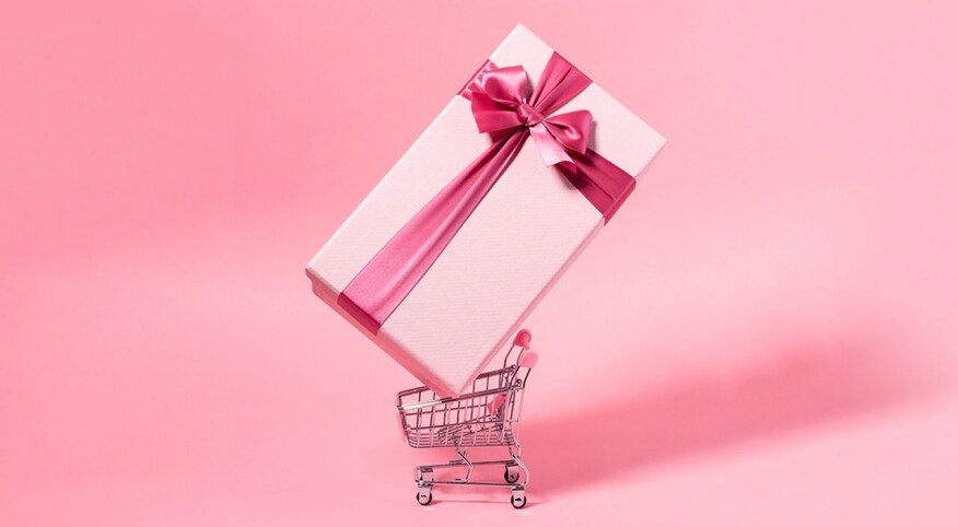 Shopping cart with giant pink gift with pink bow on pink background