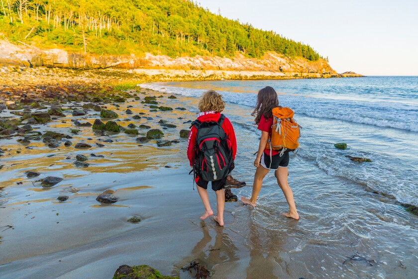 A teenage boy and girl walk on Sand Beach after a hike in Maines Acadia National Park.