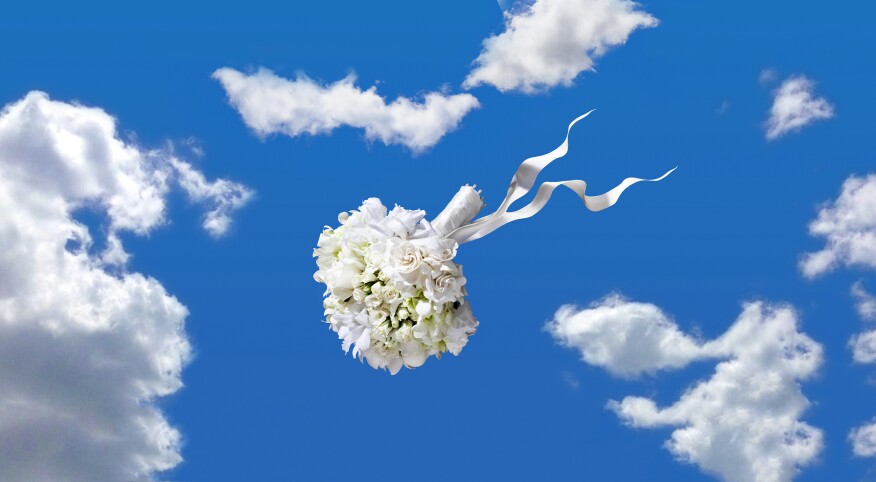 wedding bouquet being thrown through the air with clouds and blue sky behind it