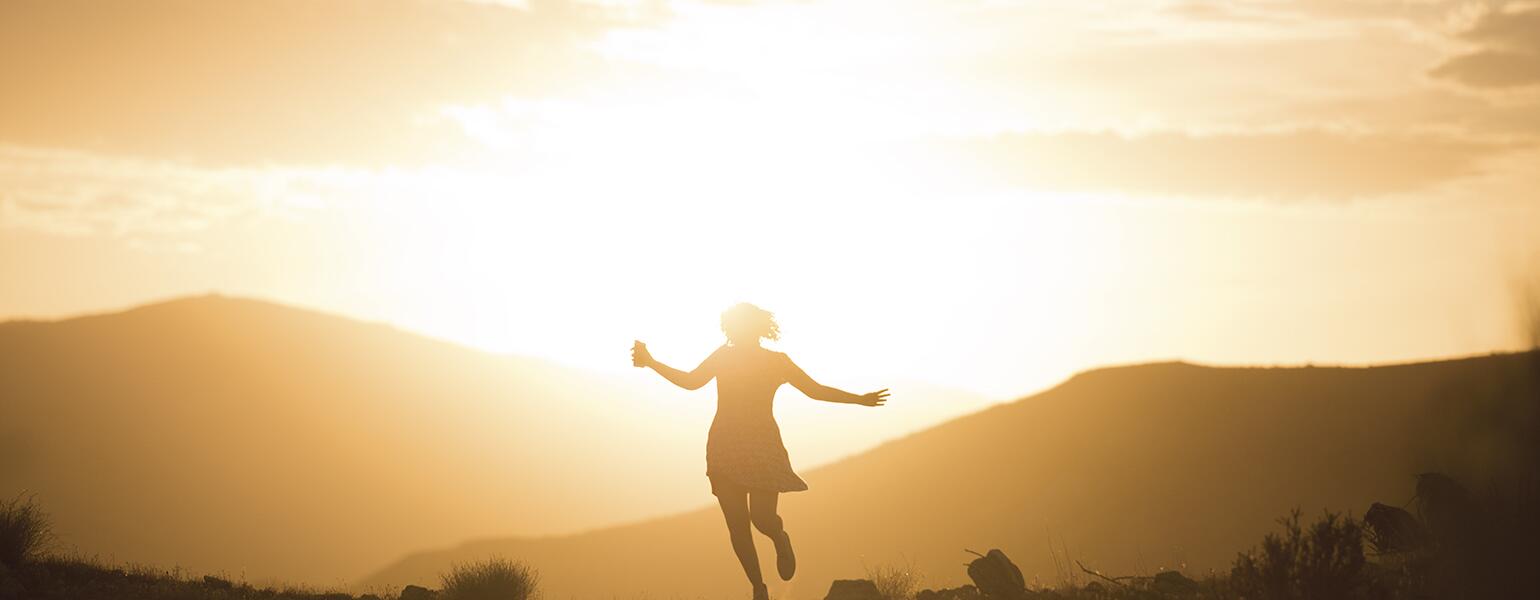 An image of a woman running carefree in the sunrise.