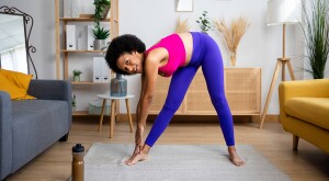 Woman at home bending down to her toes in bright workout clothes