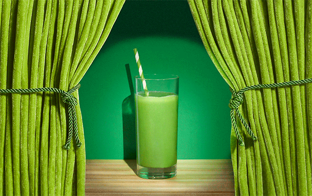 Glass of green juice on a stage with veggies peaking in and out