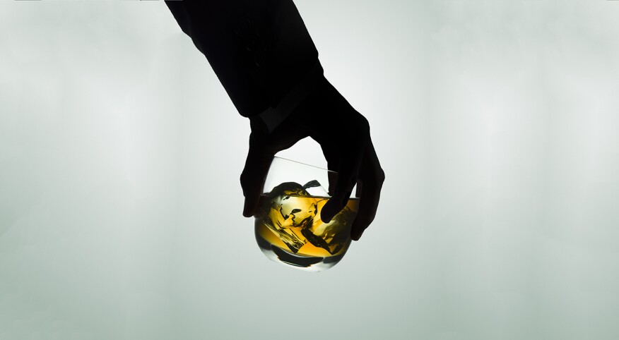 Silhouetted male hand holding a glass of whiskey