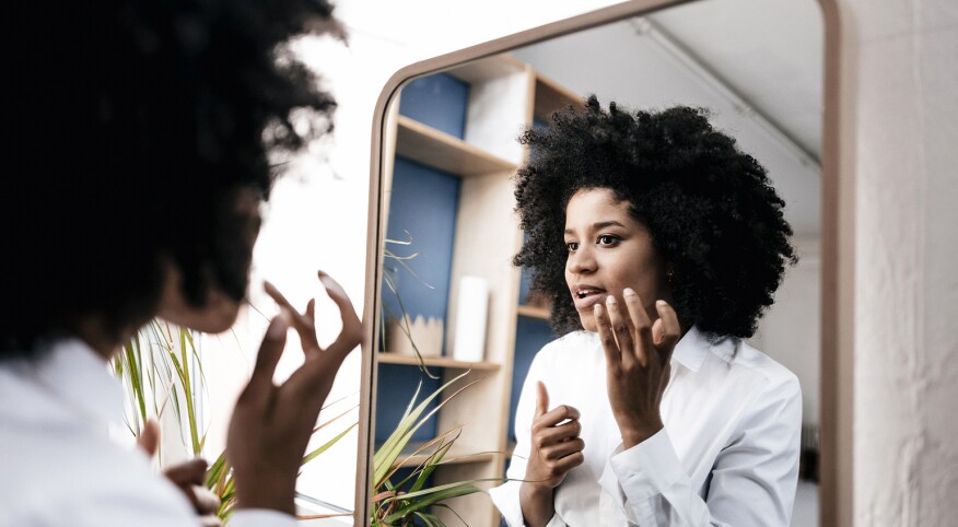 Woman looking in mirror at a dark spot on her face.