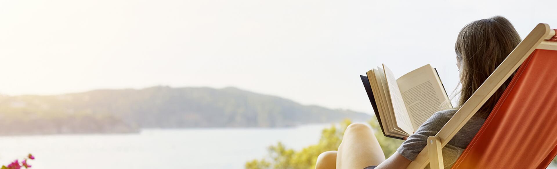 Woman reading book while relaxing on deck chair