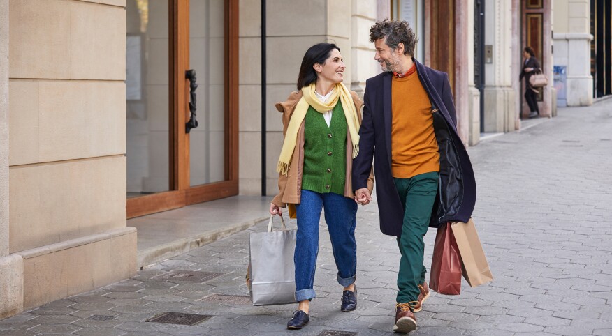 Happy couple with shopping bags talking while walking on sidewalk