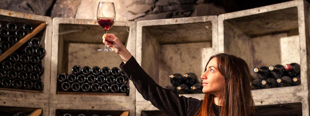 Woman raising a wine glass against in a wine cellar