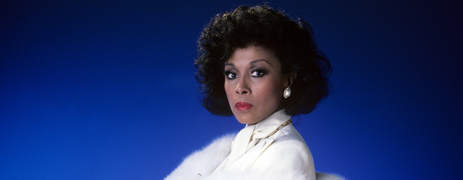 Diahann Carroll on blue background in white suit from TV show Dynasty