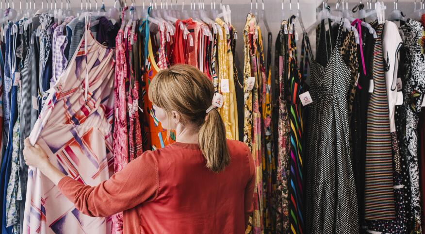 Woman looking at dress hanging on rack while standing at store