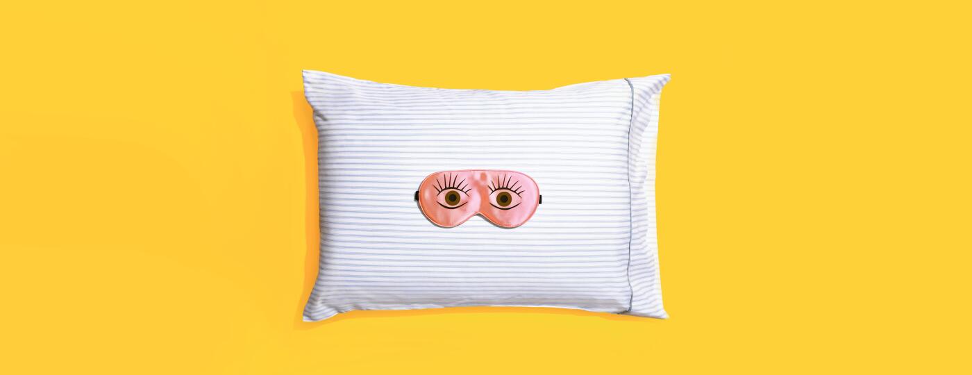 Sleeping mask on a striped pillow and yellow background
